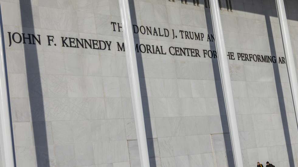 epa12605254 People walk by new signage showing US President Donald J. Trump's name above former President John F. Kennedy's on the John F. Kennedy Memorial Center for the Performing Arts building, in Washington, DC, USA, 20 December 2025. Kennedy Center's board of trustees, hand-picked by President Trump, voted to rename the institution 'The Donald J. Trump and The John F. Kennedy Memorial Center for the Performing Arts.' While the center has already updated its branding and building signage, a formal name change would likely require an Act of Congress.  EPA/SHAWN THEW