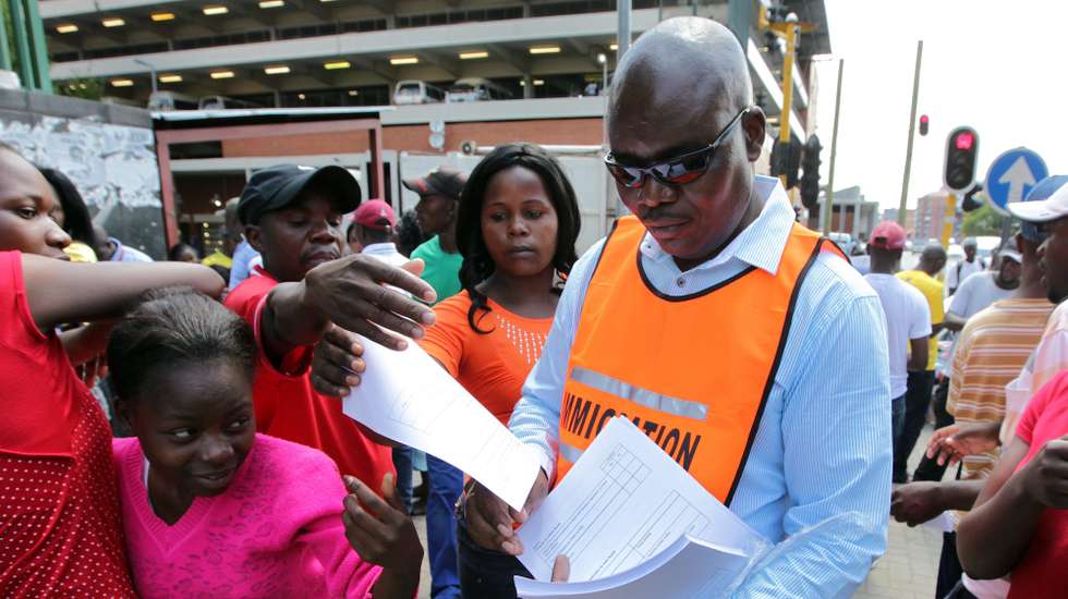 epa02508629 Exiled Zimbabwean nationals living in neighbouring South Africa clamour for registration documents from an immigration officer at the offices of the South African Department of Home Affairs in downtown Johannesburg, South Africa, 28 December 2010. Zimbabweans living illegally in South Africa have until 31 December to apply for legal residency and to submit fraudulently acquired South African documents to the South African authorities. South Africa is home to an estimated five million illegal immigrants, including some three million Zimbabweans.  EPA/JON HRUSA