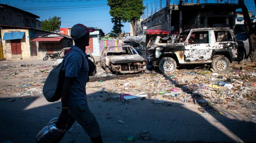 epa11209907 A man walks in front of burned vehicles due to violence in Port-au-Prince, Haiti, 09 March 2024. Suspected criminals were killed by the Haitian National Police during an attack on the National Palace on 08 March orchestrated by the 'Vivre Ensemble' coalition of armed gangs, according to local media published on 09 March.  EPA/JOHNSON SABIN