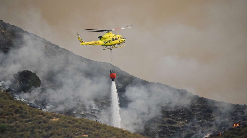 epa13102080 A fire service helicopter drops water onto one of the hotspots of the wildfire that broke out in Los Gallardos, Almeria, Spain, 10 July 2026. At least 12 people have died and 19 others are missing in a forest fire that broke out in evening of 09 July near Almeria in Andalusia, according to Andalusia's regional president Juanma Moreno.  EPA/CARLOS BARBA