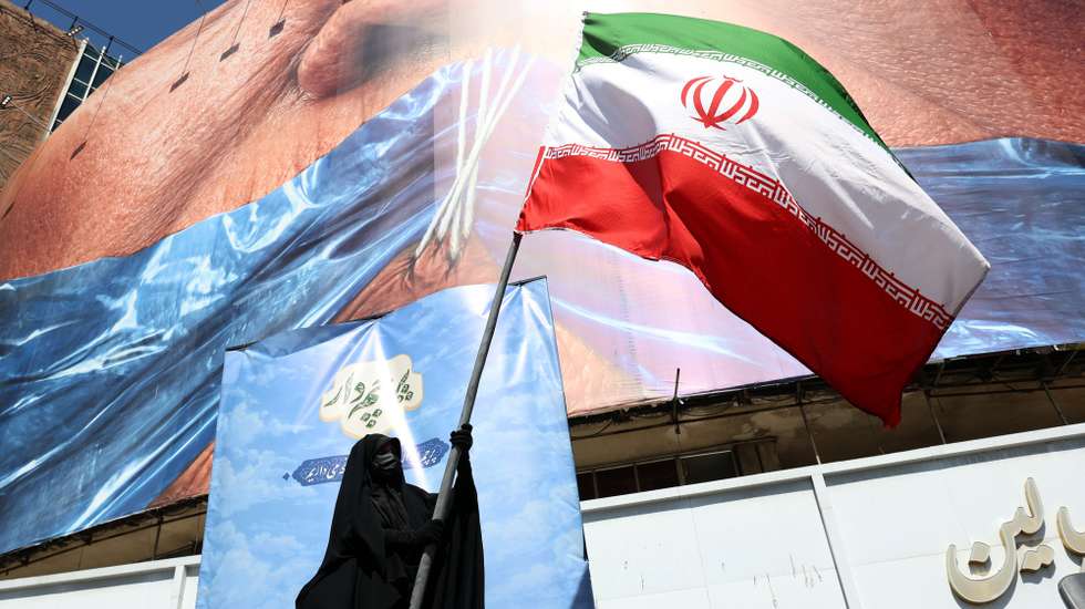 epa12946980 A veiled woman holds Iran’s national flag in front of a huge anti-US billboard referring to US President Donald Trump and the Strait of Hormuz at Valiasr Square in Tehran, Iran, 11 May 2026. US President Donald Trump says Iran’s counter-proposal to end the ongoing conflict is not acceptable.  EPA/ABEDIN TAHERKENAREH