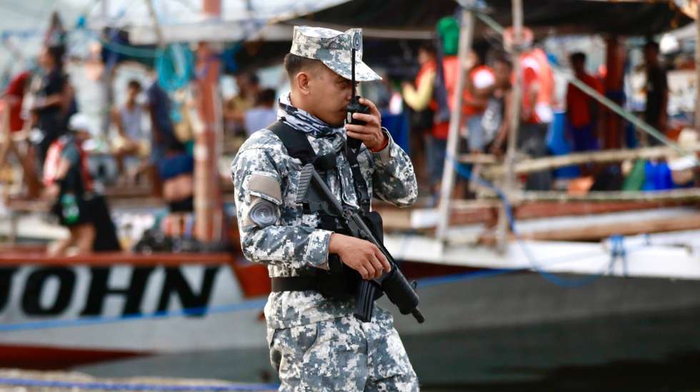 epa11340974 An armed Filipino coastguard personnel holds a radio as he stands guard next to a motorized wooden boat before they sail along Masinloc Bay on their voyage to Scarborough shoal, in the vicinity of Masinloc town, Zambales province, Philippines, 15 May 2024. A civilian-led mission joined by at least a hundred fishermen embarked on Scarborough Shoal in the disputed South China Sea to assert the Philippines’ territorial claim. Scarborough Shoal (‘Bajo de Masinloc’ called by Filipino fishermen), a fishing haven shoal within the Philippine maritime territory that China occupied a decade ago, was recently reported to be driving away Filipino fishermen by Chinese coastguard ships.  EPA/FRANCIS R. MALASIG