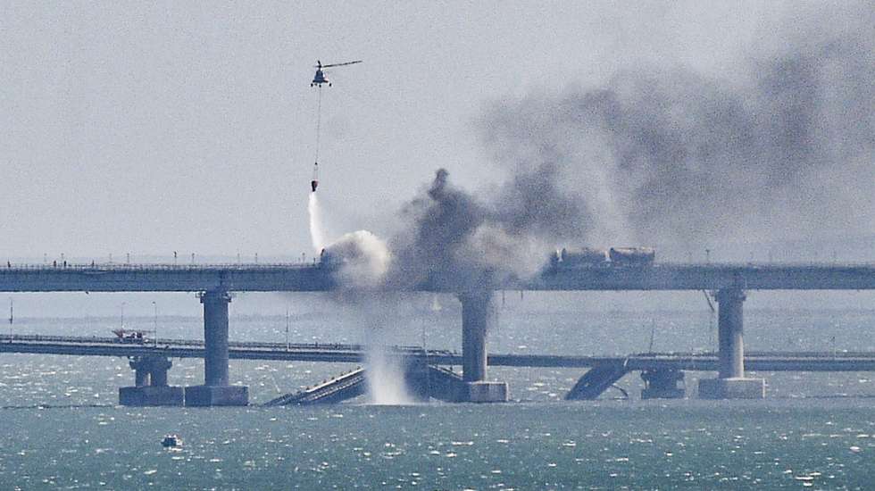 epaselect epa10230640 A firefighter helicopter pours water on fire on a collapsed part of the Kerch Strait bridge in Crimea, 08 October 2022. According to Russian authorities, "an explosion was set off at a cargo vehicle on the motorway part of the Crimean bridge on the side of the Taman peninsula, which set fire to seven fuel tanks of a train that was en route to the Crimean peninsula. Two motorway sections of the bridge partially collapsed."  EPA/STRINGER