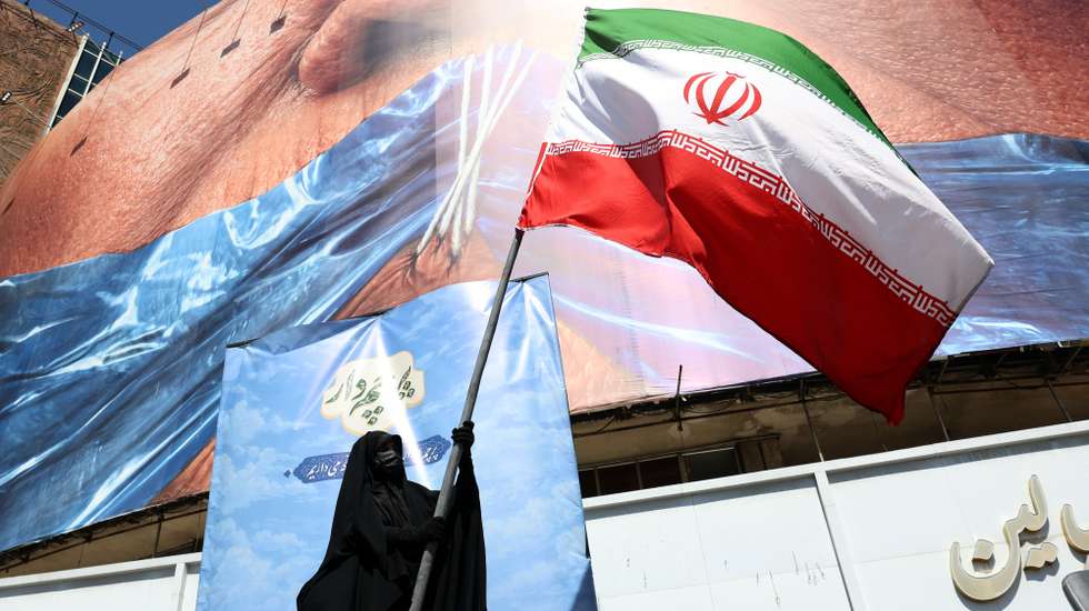 epa12946980 A veiled woman holds Iran’s national flag in front of a huge anti-US billboard referring to US President Donald Trump and the Strait of Hormuz at Valiasr Square in Tehran, Iran, 11 May 2026. US President Donald Trump says Iran’s counter-proposal to end the ongoing conflict is not acceptable.  EPA/ABEDIN TAHERKENAREH