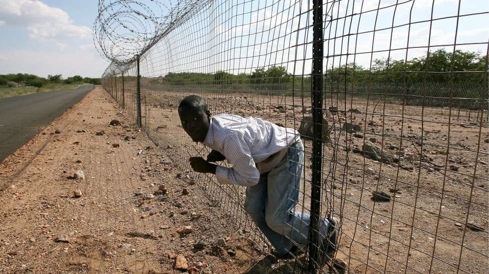 epa08306850 (FILE) An illegal immigrant struggles to climb through the electrified boarder fence between South Africa and Zimbabwe, Messina, South Africa, 18 April 2007 (reissued 19 March 2020). The South African government announced on 19 March 2020 that it would repair the fence at the Beitbridge border separating South Africa from Zimbabwe. The move comes after a pronouncement by President Cyril Ramaphosa that some of the country's ports, should be secured immediately .The fence stretches over 40 km, will now be repaired at a cost of R37 million and should be completed within a month.  EPA/KIM LUDBROOK