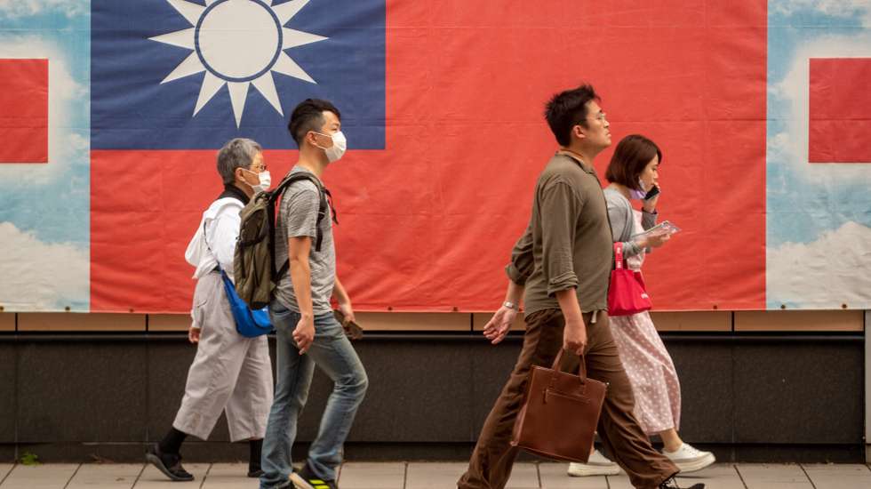 epa10561206 People walk next to a Taiwanese flag, in Taipei, Taiwan, 06 April 2023. The meeting between US House Speaker Keven McCarthy and Taiwan President Tsai Ing-wen on 05 April in the United States was deemed 'crossing the red line' by the China Foreign Affairs Committee of the National People's Congress.  EPA/RITCHIE B. TONGO