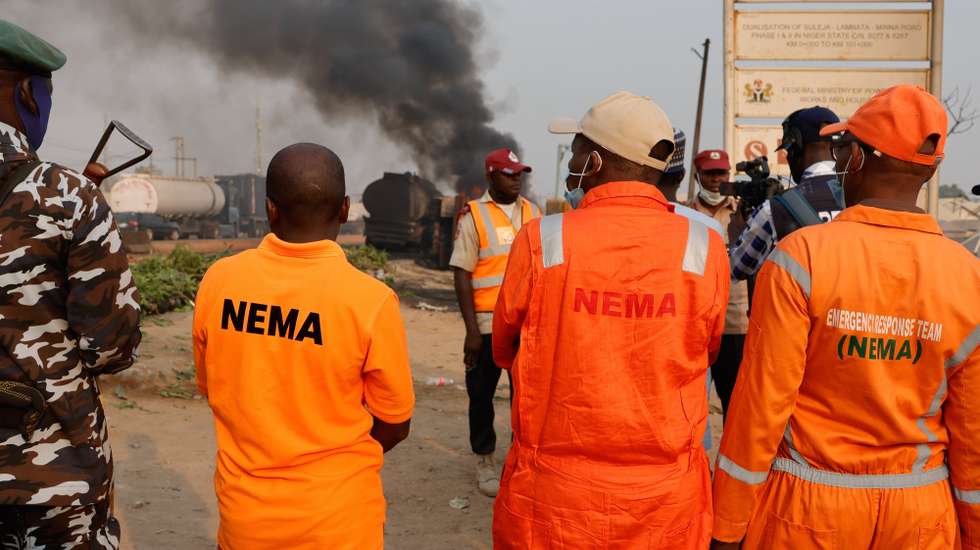 epa11834752 Members of the National Emergency Management Agency (NEMA) stand near the wreckage of a fuel tanker that burns at the Dikko junction, a road linking Abuja to Kaduna, Nigeria, 18 January 2025. According to the National Emergency Agency, over 78 burned bodies were recovered at the scene after the fuel tanker overturned and spilled the cargo, killing people who had gathered to take the spilled fuel.  EPA/AFOLABI SOTUNDE