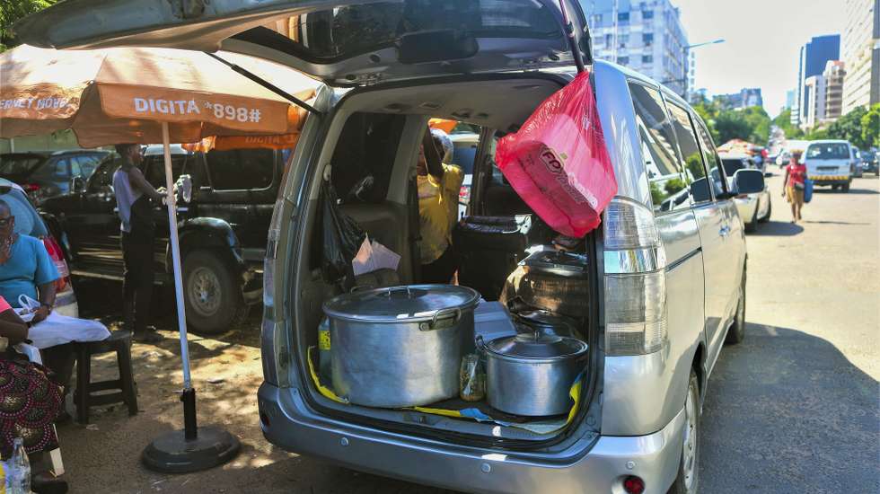 Um vendedor ambulante vende comida exposta na mala de um carro numa rua de Maputo, Moçambique, 28 de março de 2025. Chegam às primeiras horas do dia, estacionam o carro em locais centrais de Maputo e de mala aberta estes vendedores informais conseguem o sustento para a casa, servindo refeições na rua a preços de saldo. (ACOMPANHA TEXTO DA LUSA DO DIA 07 DE ABRIL DE 2025). LUÍSA NHANTUMBO/LUSA