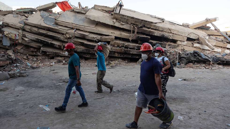 epa13072580 People walk past the rubble of a building in La Guaira, Venezuela, 29 June 2026. National and international rescue teams continue their efforts among the ruins of buildings in the coastal state of La Guaira, north of Caracas, the epicentre of devastation caused by 7.2- and 7.5-magnitude earthquakes, where logistics centres for international teams have been set up.  EPA/RONALD PENA R