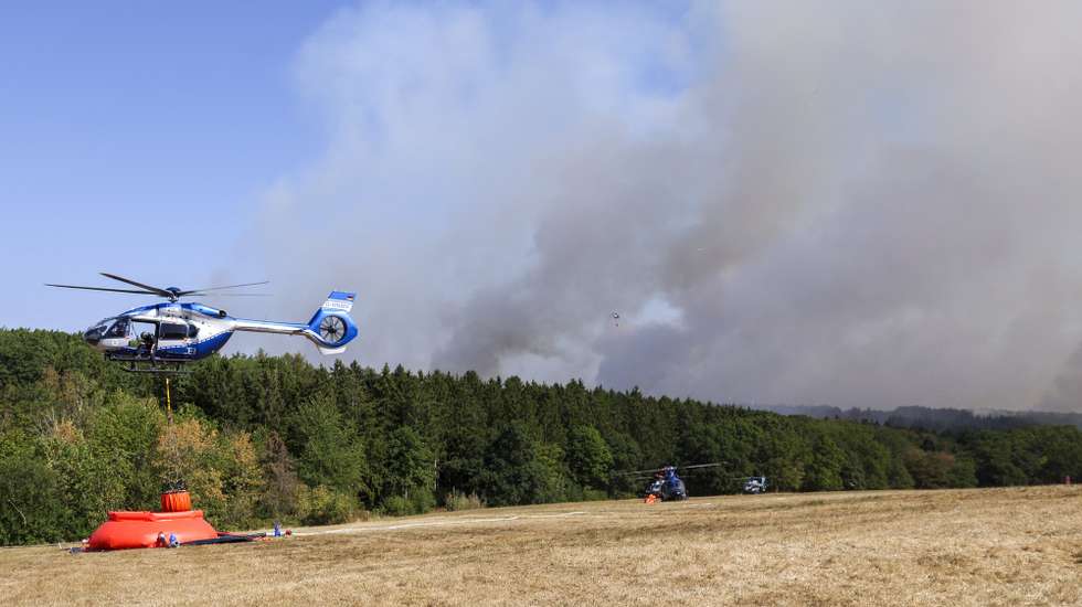 epa13168894 A police helicopter assists to extinguish the wildfire at the Huertgenwald near Dueren, Germany, 14 August 2026. The fire brigade is battling a forest fire in the Dueren district of North Rhine-Westphalia. As the fire is drawing closer to the village of Huertgenwald, 1,800 people have already been evacuated.  EPA/CHRISTOPHER NEUNDORF