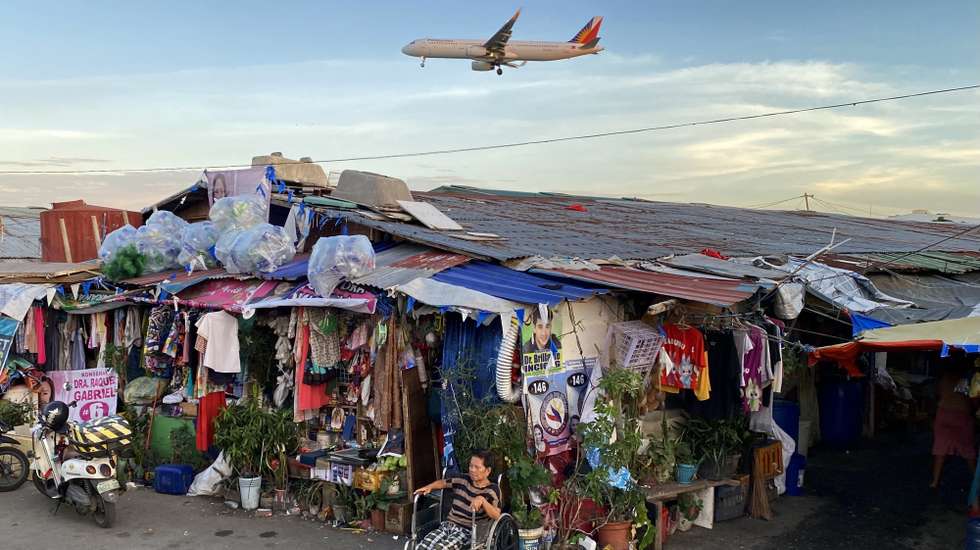 epa11944074 An elderly woman sits next to shanties as a Philippine Airlines (PAL) plane flies over a slum area in Paranaque city, Metro Manila, Philippines, 06 March 2025. According to the latest report of the Philippine Statistics Authority (PSA), poverty rate dropped to 15.5 percent in 2024 from 18.1 percent in 2021, with 17.54 million people living below the poverty line, a decrease of 2.4 million from the previous survey two years earlier.  EPA/FRANCIS R. MALASIG