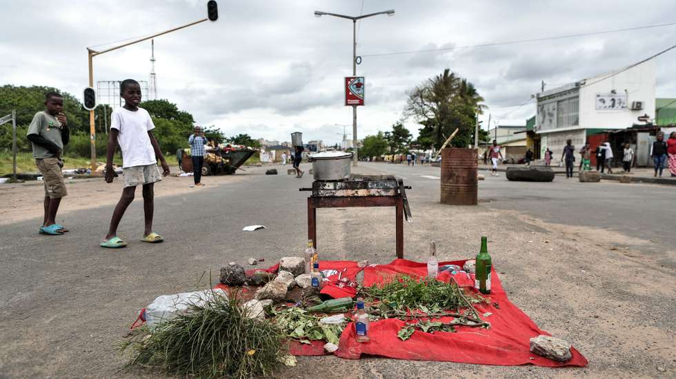 Crianças observam um fogao improvisado numa estrada bloqueada em Maputo, Moçambique, 28 de novembro de 2024. Barricadas tomaram conta hoje de Maputo, com ruas e avenidas centrais praticamente sem viaturas, ocupadas por manifestantes, pedras, contentores do lixo, ferros, paus e tudo o que permita bloquear a passagem, em mais uma ação de protesto pós-eleitoral. LUISA NHANTUMBO/LUSA