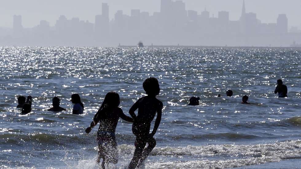 epaselect epa09284687 Children run along the water at Alameda Beach with the San Francisco City skyline in the background in Alameda, California, USA, 18 June 2021. Temperatures reached 41 degrees celsius in the inland parts of the San Francisco Bay Area.  EPA/JOHN G. MABANGLO