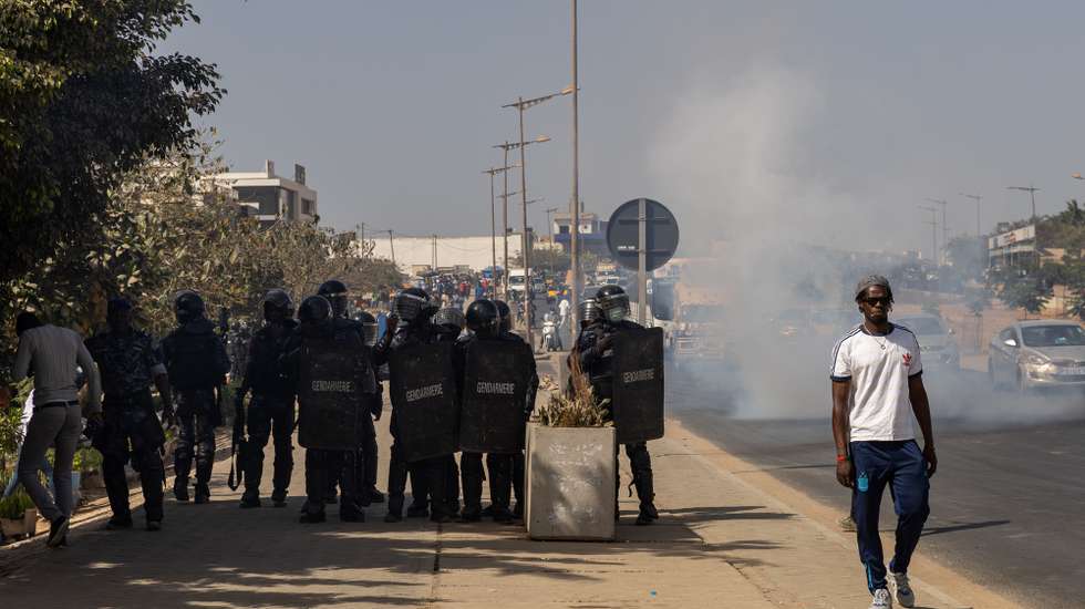 epa11126649 A man walks past police officers and a cloud of tear gas in Dakar, Senegal, 04 February 2024. On 03 February, Senegal's President Macky Sall announced in a televised speech the postponement of presidential elections scheduled for 25 February without setting a new date. Several opposition figures rejected the decision to postpone the election, with some of them wowing to proceed with their campaign originally scheduled to kick off on 04 February.  EPA/JEROME FAVRE