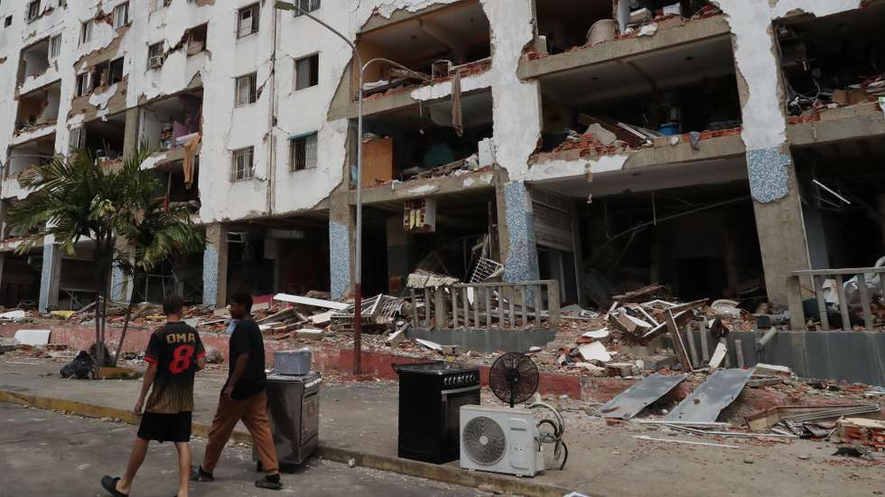epa13086363 People walk past buildings damaged by the earthquakes in the Caraballeda area of La Guaira, Venezuela, 04 July 2026. Venezuela is assessing damage to the country's infrastructure while attempting to accelerate debris-removal efforts, ten days after devastating earthquakes left at least 2,645 people dead and as the chances of rescuing survivors dwindle to a minimum.  EPA/Raul Martinez