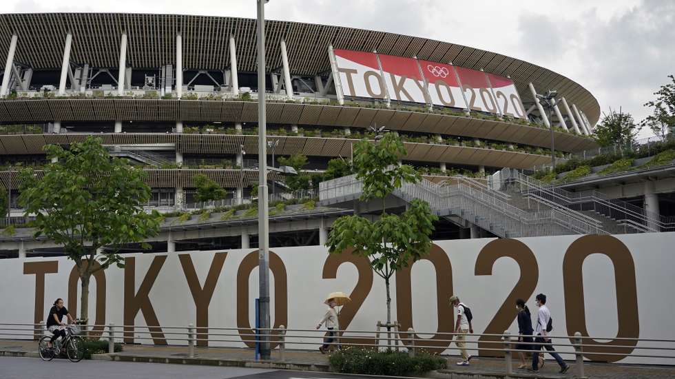 epa09294866 Passersby walk past the National Stadium, the main stadium of the 2020 Tokyo Olympic Games, in Tokyo, Japan, 23 June 2021, one month before the opening of the Tokyo 2020 Olympic Games. The National Stadium will host the opening, closing ceremonies and the athletics events. The Summer Games were postponed due to COVID-19 Coronavirus pandemic.  EPA/FRANCK ROBICHON