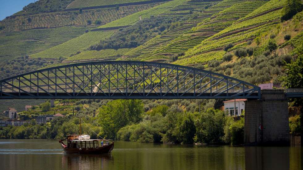 Um barco de uma operadora de turismo do Douro passa com turistas a bordo pela ponte do Pinhão, Vila Real, 05 de junho de 2020. Várias empresas marítimo-turísticas estão instaladas na vila do Pinhão, concelho de Alijó, distrito de Vila Real. As embarcações atracadas no cais, desde veleiros a barcos rabelo, esperam pelos turistas que, nos anos anteriores, invadiam este território provenientes dos mais diferentes países. (ACOMPANHA TEXTO DA LUSA DO DIA 08 DE JUNHO DE 2020). PEDRO SARMENTO COSTA/LUSA