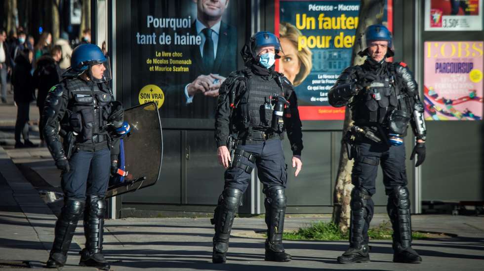 epa09750515 French police officers stand guard on the Champs Elysees in front of a press cover poster displaying a portrait of French President Macron as participants in a so-called 'Freedom Convoy' are trying to block the traffic, in Paris, France, 12 February 2022. Paris police have prohibited the convoy, as announced by the capital's prefect on 10 February. A series of convoy demonstrations has been taking place in France to call for the lifting of all Covid-19-related restrictions and mandates, in light of the ongoing protest in Canada, where truck drivers have been rallying against the government-imposed mandatory Covid-19 vaccine to enter the country.  EPA/CHRISTOPHE PETIT TESSON