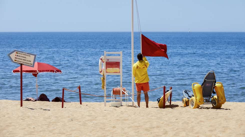 Um nadador-salvador da praia de Quarteira retira a bandeira vermelha, que interditava os turistas a banhos devido à presença de bactérias prejudiciais à saúde na água do mar, para hastear a bandeira verde que permite os banhos, após nova análise à qualidade da água nas praias de Quarteira e Vale do Lobo, em Loulé, 26 de julho de 2023. A interdição a banhos nas praias de Quarteira e Vale do Lobo, no Algarve, que durou menos de 24 horas e cuja interdição foi hoje levantada, foi causada por um foco de poluição. RICARDO NASCIMENTO/LUSA