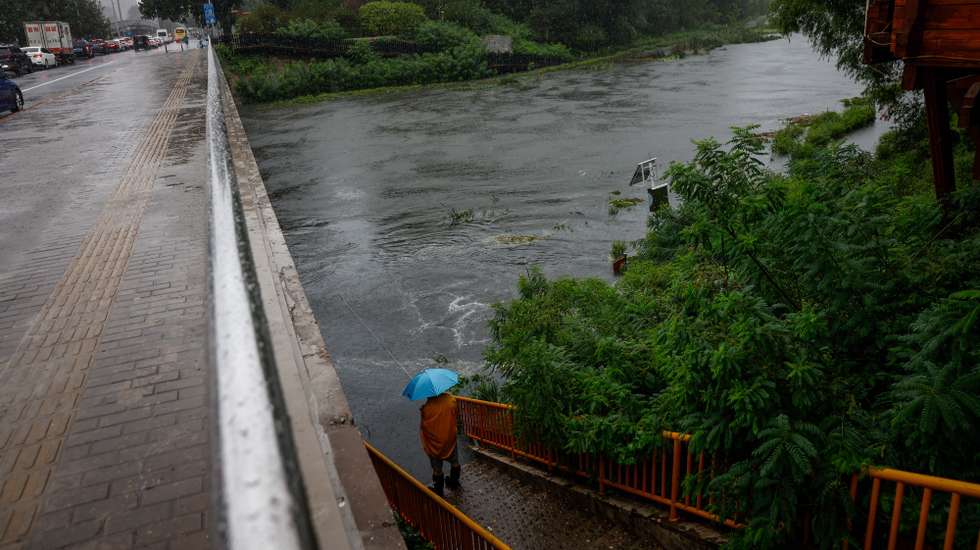 epa10776429 A man fishes along a swelling river in Beijing, China, 30 July 2023. China's National Meteorological Center issued a red alert, the highest alert in multiple provinces including Beijing, as the country is expected to continue experiencing heavy rainfall brought by Typhoon Doksuri.  EPA/MARK R. CRISTINO