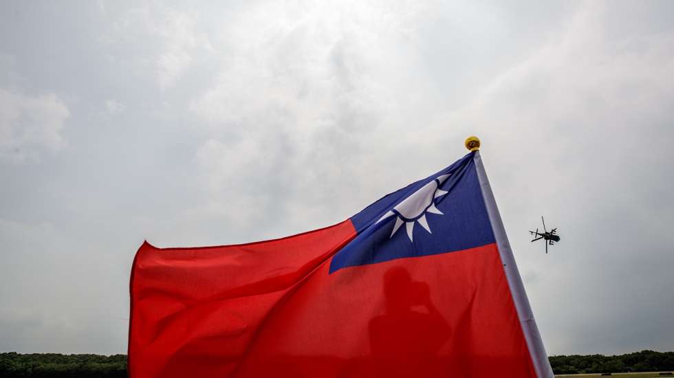 epa10873506 A person looks on from behind the Taiwan national flag as an AH-64 Apache helicopter maneuvers during an anti-invasion drill inside a military base in Hsinchu county, Taiwan, 21 September 2023. On 18 September, the Taiwanese military detected nine warships and 103 military aircraft from China near Taiwan. Taiwan's Ministry of National Defense has demanded that China cease its 'unilateral military harassment'.  EPA/RITCHIE B. TONGO