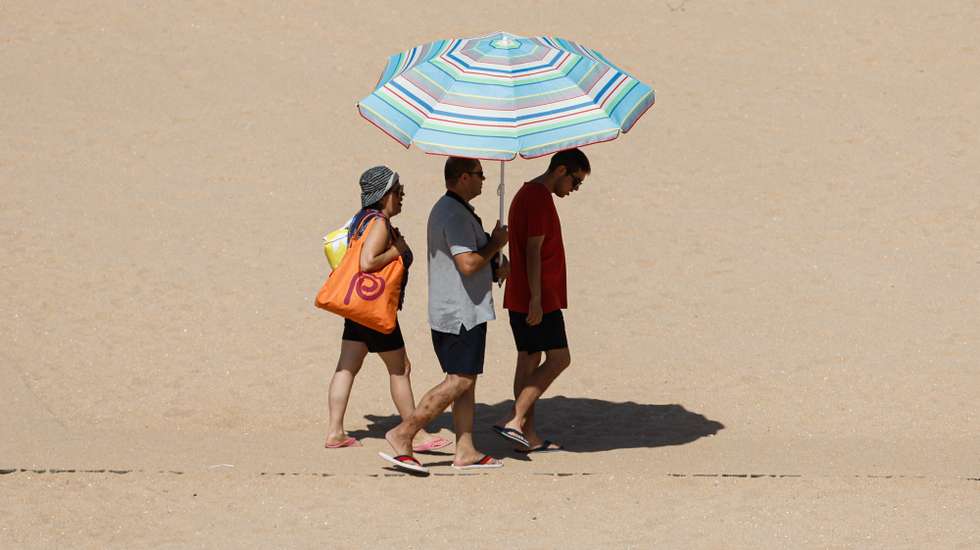 Turistas protegem-se do sol com um guarda-sol numa praia em Albufeira, 22 de agosto de 2023. Por causa do tempo quente, o IPMA colocou os distritos de Vila Real, Bragança, Viseu, Guarda, Coimbra, Castelo Branco e Santarém sob aviso vermelho entre as 00:00 de hoje e as 10:00 de quinta-feira. LUÍS FORRA/LUSA