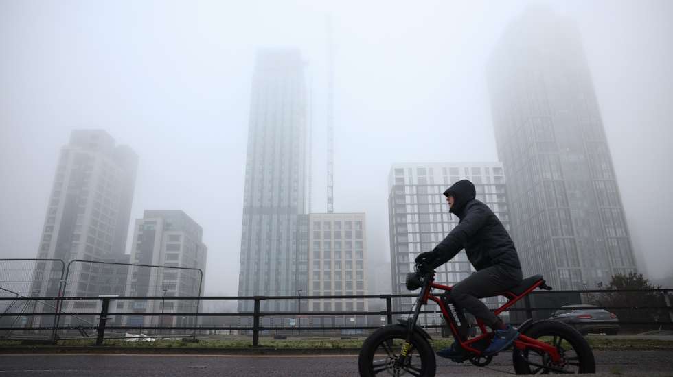 epa11794883 A cyclist passes buildings shrouded in heavy fog in Liverpool, Britain, 27 December 2024. Heavy fog has caused disruption including flight delays and football match cancellations, with the Met Office predicting it could remain into the weekend.  EPA/ADAM VAUGHAN