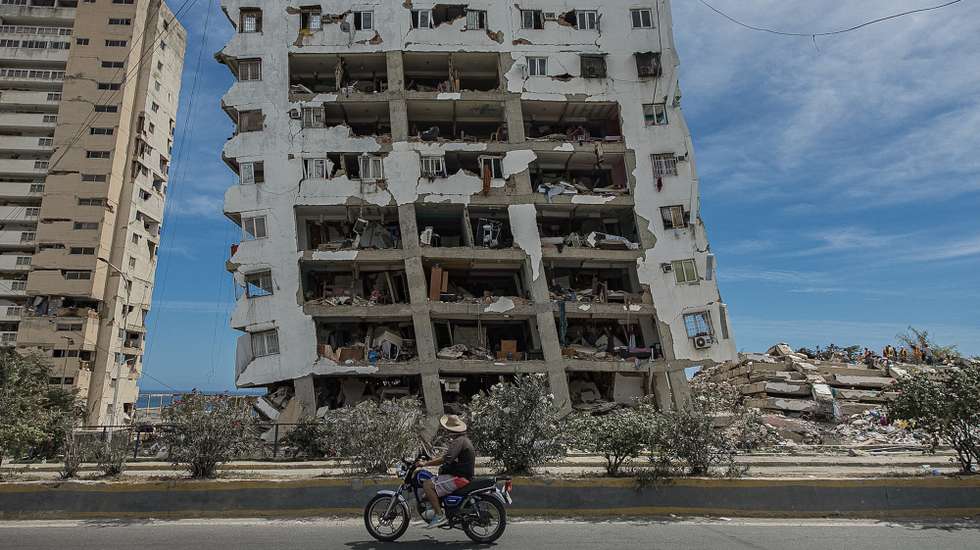 epa13070939 A person walks past a building destroyed by the earthquakes in Catia La Mar, Venezuela, 28 June 2026. Venezuelan National Assembly President Jorge Rodriguez said at least 1,430 people were killed after two powerful earthquakes struck the country on 24 June. Authorities have restricted access to some disaster zones and deployed the military as relief efforts continue.  EPA/Henry Chirinos