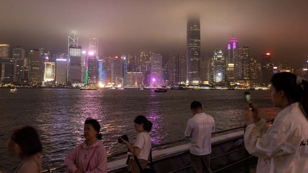 epa10542524 People look at lilluminated buildings across Victoria Harbour on Hong Kong island a few minutes before Earth Hour in Hong Kong, China, 25 March 2023. During Earth Hour many buildings along the Victoria Harbour waterfront switch off their lights and go dark for an hour. Earth Hour was originally started in 2007 in Sydney by the World Wildlife Fund and is now a global movement in which millions participate to demonstrate the need for greater action on climate change and energy saving.  EPA/JEROME FAVRE