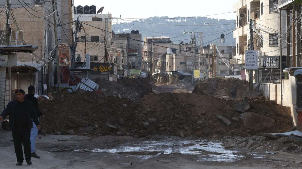 epa11963979 Palestinians walk near debris at a blocked road during an Israeli military operation in the West Bank city of Jenin, 14 March 2025. The Israeli military launched a military operation in Jenin and its camp on 21 January, resulting in at least 34 Palestinian deaths and dozens of injuries, according to the Palestinian Ministry of Health.  EPA/ALAA BADARNEH