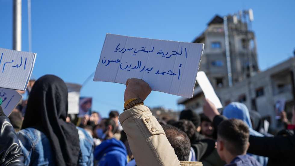 epa12615378 A protester holds a banner reading in Arabic 'freedom to Grand Mufti of Syria  Ahmad Badreddin Hassoun' as members of the Alawite community gather to protest violence against Alawites following the Homs mosque bombing, in the city of Latakia, Syria, 28 December 2025. The protesters gathered against attacks targeting the Alawite community after a bombing at the Imam Ali bin Abi Talib Mosque in an Alawite neighborhood of Homs province on 26 December, in which at least eight people were killed and more than a dozen injured.  EPA/AHMAD FALLAHA