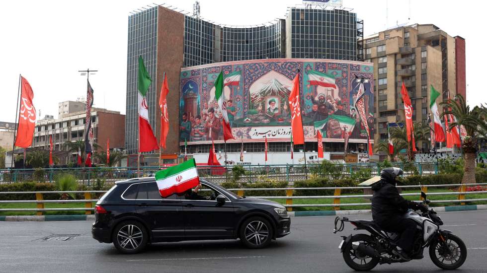 epa12861685 A vehicle adorned with the Iranian national flag drives past a large-scale political banner at the Valiasr square in Tehran, Iran, 31 March 2026. A joint US and Israeli military operation, launched on 28 February, continues to target strategic sites across Iran.  EPA/ABEDIN TAHERKENAREH