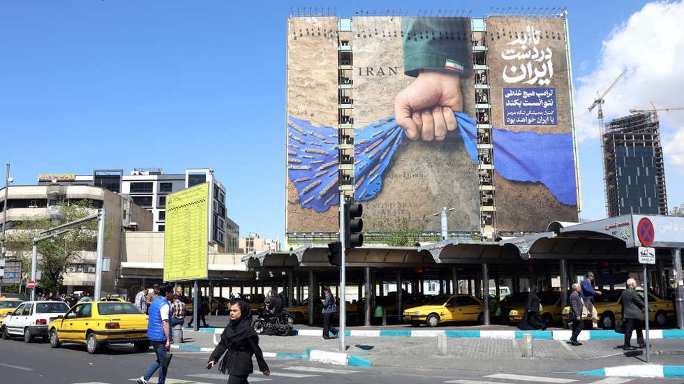 epa12891311 Iranians cross the street in front of a large-scale billboard referring to the Strait of Hormuz and reading in Persian 'Forever on Iran's hand' is displayed at a square in Tehran, Iran, 15 April 2026. After failed negotiations in Islamabad, US President Trump directed the US Navy to implement a blockade of Iranian ports in the Strait of Hormuz to halt Iran's maritime trade.  EPA/ABEDIN TAHERKENAREH
