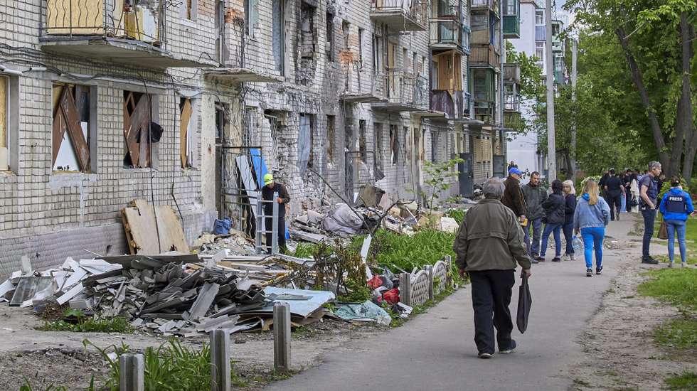 epa09974733 Locals walk past a residential building that was damaged during shelling in the outskirts of Kharkiv, Ukraine, 25 May 2022. Ukraine's second-largest city Kharkiv and its surroundings witnessed repeated airstrikes from Russian forces. On 24 February, Russian troops invaded Ukrainian territory starting a conflict that has provoked destruction and a humanitarian crisis. According to the UNHCR, more than 6.5 million refugees have fled Ukraine, and a further 7.7 million people have been displaced internally within Ukraine since.  EPA/SERGEY KOZLOV