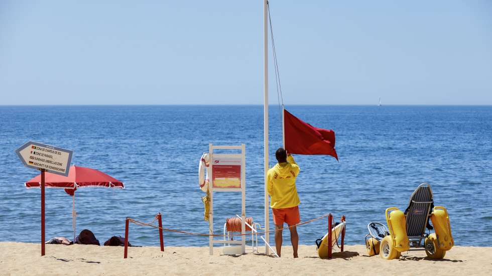 Um nadador-salvador da praia de Quarteira retira a bandeira vermelha, que interditava os turistas a banhos devido à presença de bactérias prejudiciais à saúde na água do mar, para hastear a bandeira verde que permite os banhos, após nova análise à qualidade da água nas praias de Quarteira e Vale do Lobo, em Loulé, 26 de julho de 2023. A interdição a banhos nas praias de Quarteira e Vale do Lobo, no Algarve, que durou menos de 24 horas e cuja interdição foi hoje levantada, foi causada por um foco de poluição. RICARDO NASCIMENTO/LUSA
