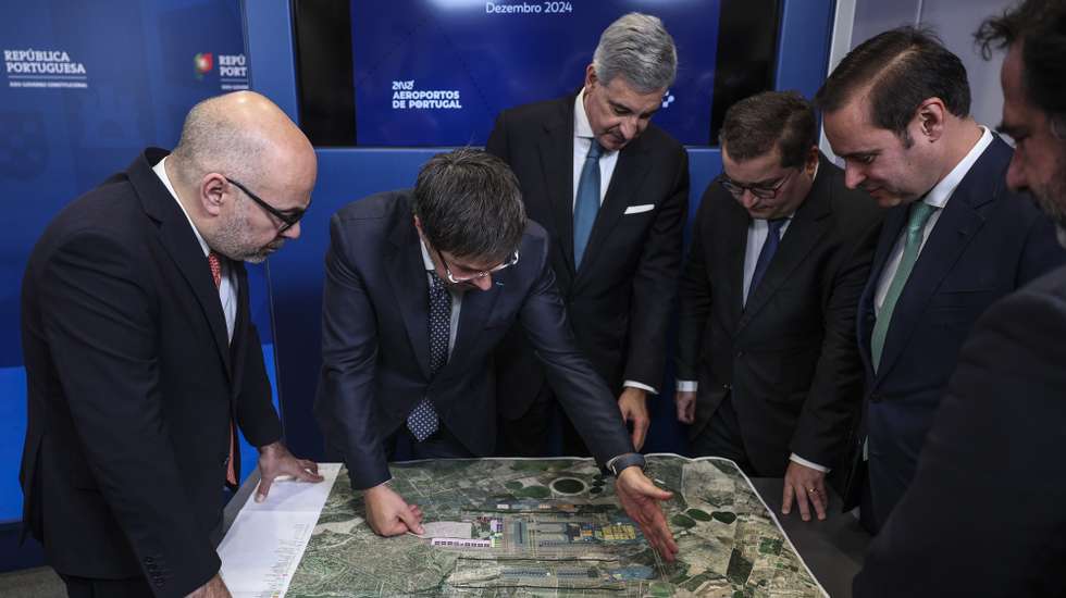 O ministro das Infraestruturas e Habitação, Miguel Pinto Luz (E), o ministro de Estado e das Finanças, Joaquim Miranda Sarmento (3-D), o presidente da ANA, José Luis Arnaut (3-E), e o presidente executivo da ANA, Thierry Ligonnière (2-E), observam o plano do aeroporto após receberem o Relatório Inicial (High Level Assumption Report) da concessionária ANA sobre o desenvolvimento da capacidade aeroportuária de Lisboa,  para iniciar formalmente negociações sobre a extensão do contrato de concessão e viabilizar a construção do novo Aeroporto Luís de Camões, em Alcochete, 17 de dezembro de 2024.  ANDRÉ KOSTERS/LUSA