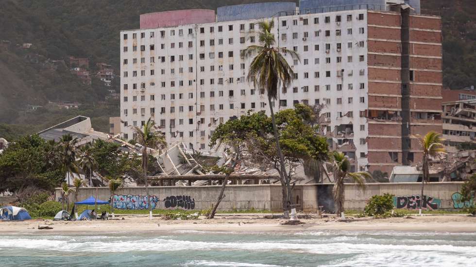 epa13158508 People rest at a beach beside a collapsed building in La Guaira, Venezuela, 09 August 2026. La Guaira is the state hardest hit by the two earthquakes that struck Venezuela on 24 June.  EPA/RONALD PENA R
