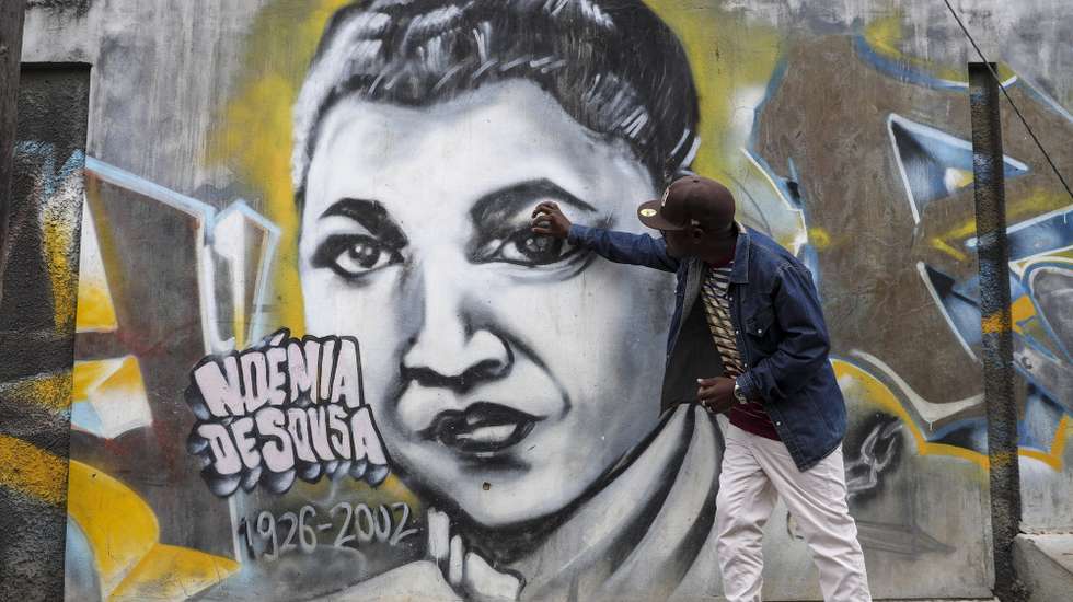O artista moçambicano Bruno Mateus, conhecido como Shot.B, posa junto ao mural dedicado à Noémia de Sousa no bairro da Mafalala, em Maputo, Moçambique, 31 de agosto de 2026. Cem anos após ter nascido, nem o mural com o rosto aviva a memória dos residentes da Mafalala, em Maputo, onde a poeta e jornalista Noémia de Sousa cresceu, entre pedidos de iniciativas para manter vivo o legado. (ACOMPANHA TEXTO DA LUSA DO DIA 31 DE AGOSTO DE 2026). LINA CEBOLA/LUSA.