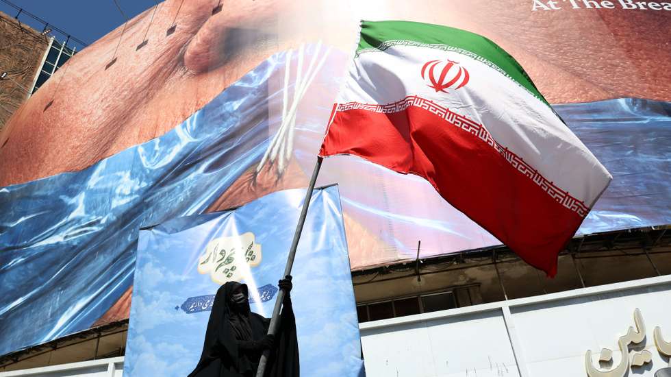 epa12946980 A veiled woman holds Iran’s national flag in front of a huge anti-US billboard referring to US President Donald Trump and the Strait of Hormuz at Valiasr Square in Tehran, Iran, 11 May 2026. US President Donald Trump says Iran’s counter-proposal to end the ongoing conflict is not acceptable.  EPA/ABEDIN TAHERKENAREH