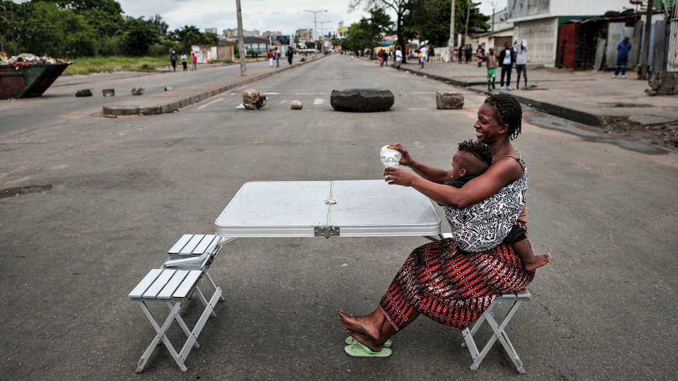 Uma mulher com o filho ao colo bebe um copo de água numa mesa colocada numa estrada bloqueada em Maputo, Moçambique, 28 de novembro de 2024. Barricadas tomaram conta hoje de Maputo, com ruas e avenidas centrais praticamente sem viaturas, ocupadas por manifestantes, pedras, contentores do lixo, ferros, paus e tudo o que permita bloquear a passagem, em mais uma ação de protesto pós-eleitoral. LUISA NHANTUMBO/LUSA