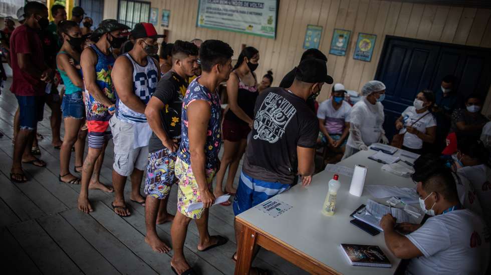 epa09231454 People wait to receive a dose of the AstraZeneca (Vaxzevria) vaccine against COVID-19, in the community of Vila do Cuinha in Anama, Brazil, 27 May 2021. Employees of the Municipal Health Secretariat of Anama arrived in Vila do Cuinha, after a 20-minute boat trip along the Solimoes River from the Anama municipality headquarters, with the aim of vaccinating 190 people, over 18 years of age, with at least the first dose of the COVID-19 immunizer. People received the vaccine at one of the community colleges.  EPA/Raphael Alves