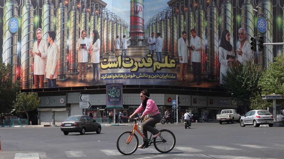 epaselect epa12342274 An Iranian woman rides a bicycle next to a billboard displaying a picture of nuclear centrifuges and a sentence reading in Persian 'Science is the power, and the Iranian nation will not abandon its religion and knowledge' at the Enghelab square in Tehran, Iran, 01 September 2025.  EPA/ABEDIN TAHERKENAREH