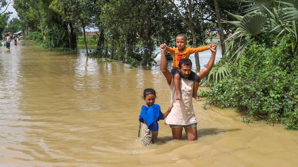 epa11565824 A man and his children ade through floodwater at a flood-affected area in Burichong, Comilla district, Bangladesh, 26 August 2024. According to the Disaster Management and Relief Ministry, at least 23 people have died and over five million have been affected by the floods triggered by heavy rain in Bangladesh.  EPA/MONIRUL ALAM