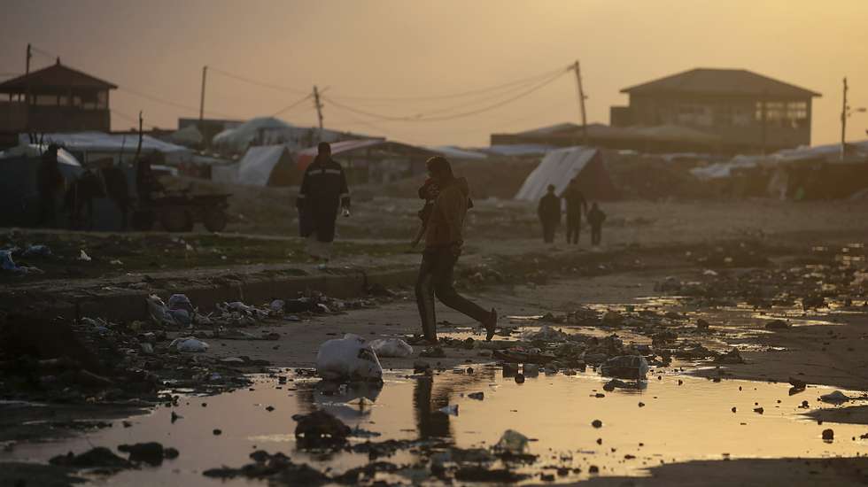 epa11114546 Displaced Palestinians who fled their houses from the northern Gaza Strip walk past a rain water puddle next to their shelters during a cold evening in Deir Al Balah town, southern Gaza Strip, 30 January 2024. More than 26,700 Palestinians and at least 1,330 Israelis have been killed, according to the Palestinian Health Ministry and the Israel Defense Forces (IDF), since Hamas militants launched an attack against Israel from the Gaza Strip on 07 October 2023, and the Israeli operations in Gaza and the West Bank which followed it.  EPA/MOHAMMED SABER