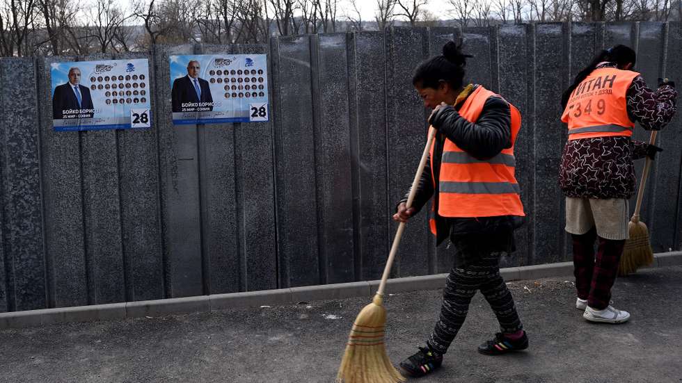 epa09108202 Cleaning employees sweep in front of campaign posters of Bulgaria's centre-right ruling GERB party with pictures of Bulgarian Prime minister Boyko Borissov in Bankaj, Bulgaria, 31 March 2021. Bulgaria will hold parliamentary elections on 04 April 2021.  EPA/VASSIL DONEV
