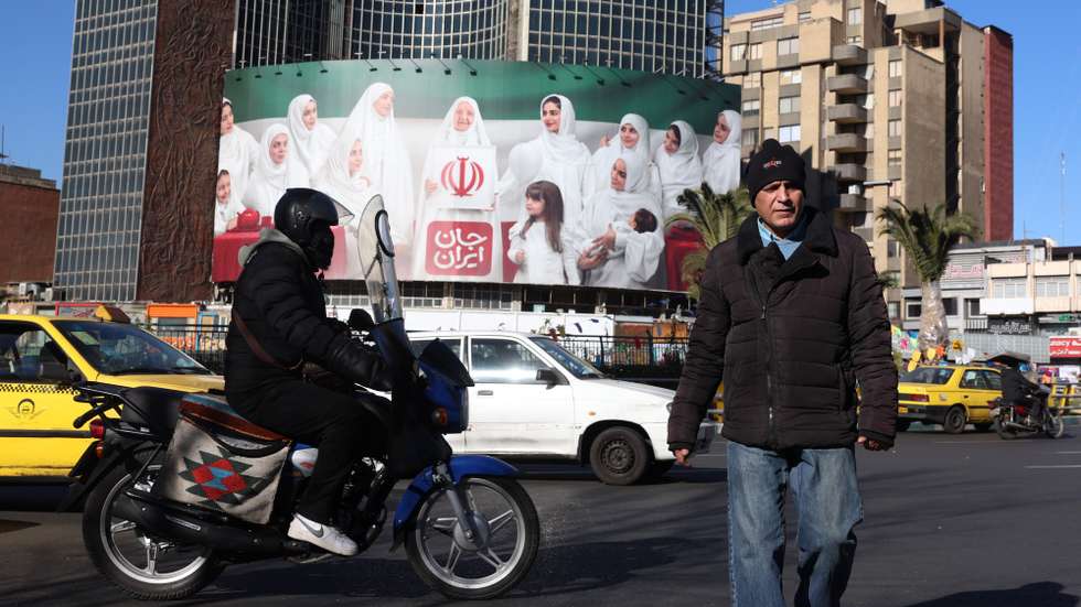 epa12616584 Iranians walk next to a huge poster in the colors of Iran's national flag in a street in Tehran, Iran, 29 December 2025. Iran is experiencing an economic crisis as the value of its currency declines as a result of tensions between Iran, Israel, and the US as well as sanctions implemented by the US and EU against Iran.  EPA/ABEDIN TAHERKENAREH