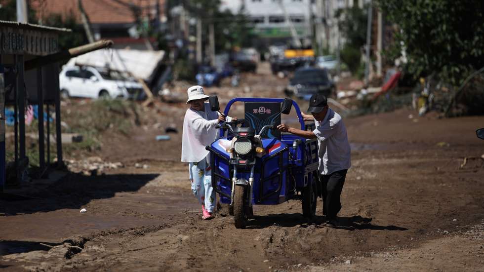 epa12272814 Two local residents push a tricycle along a street affected by flooding in a neighborhood of the district of Miyun, Beijing, China, 30 July 2025. At least 30 people have died, and thousands have been evacuated after heavy rains have caused infrastructural damage and power outages over the last days.  EPA/ANDRES MARTINEZ CASARES