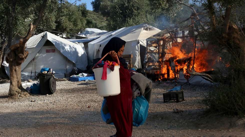 epa08763990 YEARENDER 2020 DISASTERS AND ACCIDENTSAn Asylum seeker carries possessions away from a fire in the Moria refugees camp on the island of Lesvos, Greece, 10 September 2020. A second fire broke out in the Moria refugee camp on 10 September. A passenger ferry and two Navy landing ships will accommodate about 2,000 refugees who are homeless after the fire at Moria, Migration and Asylum Minister Notis Mitarachi said. The island of Lesvos was declared in state of emergency for four months, by order of Deputy Civil Protection and Management Crises Minister Nikos Hardalias and the general secretary of civil protection Vassilis Papageorgiou. EPA/ORESTIS PANAGIOTOU