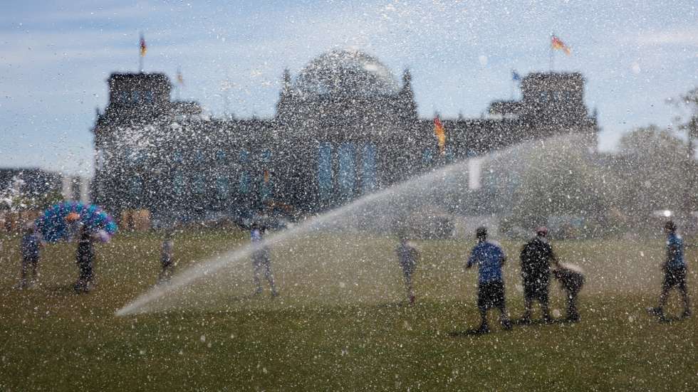 epa13060558 People are seen behind water bubbles as they move between sprinklers in front of the Reichstag building, the seat of the German parliament, during hot temperatures in Berlin, Germany, 24 June 2026. The German Weather Service forecasted strong to extreme heat stress in large parts of the country.  EPA/CLEMENS BILAN