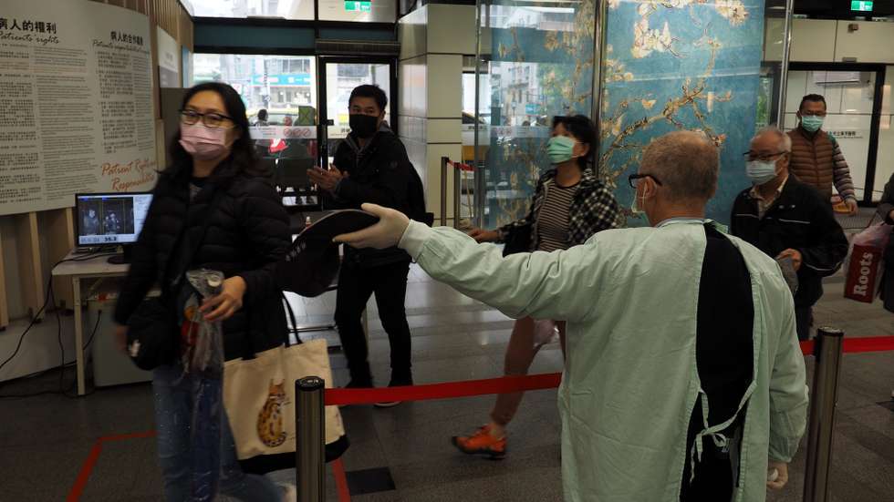 epa08877659 A man (R) wearing a medical gown makes sure all visitors wear face masks in the lobby of a hospital in Taipei, Taiwan, 11 December 2020. Taiwan has tightened measures to prevent surge of Covid-19 infection in winter.  EPA/DAVID CHANG